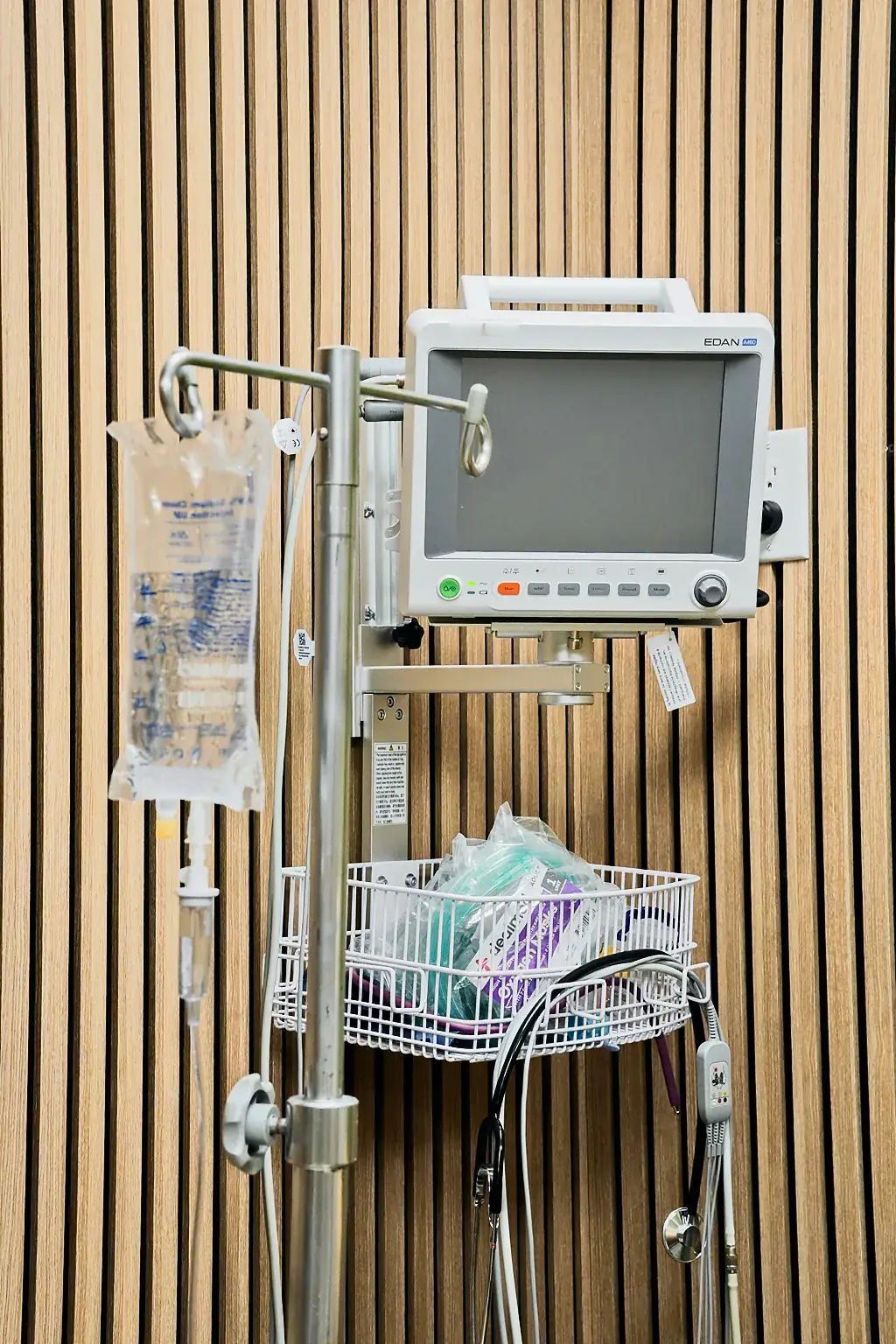 An IV pole and patient monitor against the wood-slat wall